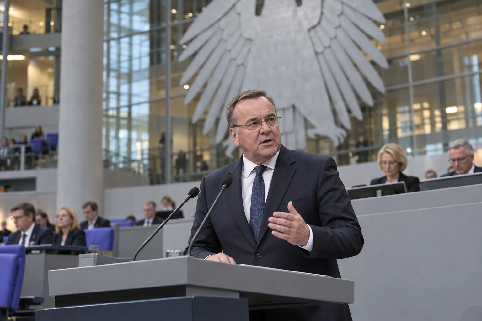 KI-generierte Illustration: Boris Pistorius am Rednerpult im Plenarsaal des Deutschen Bundestages, Bundesadler im Hintergrund, Nachrichtenfoto-Stil.