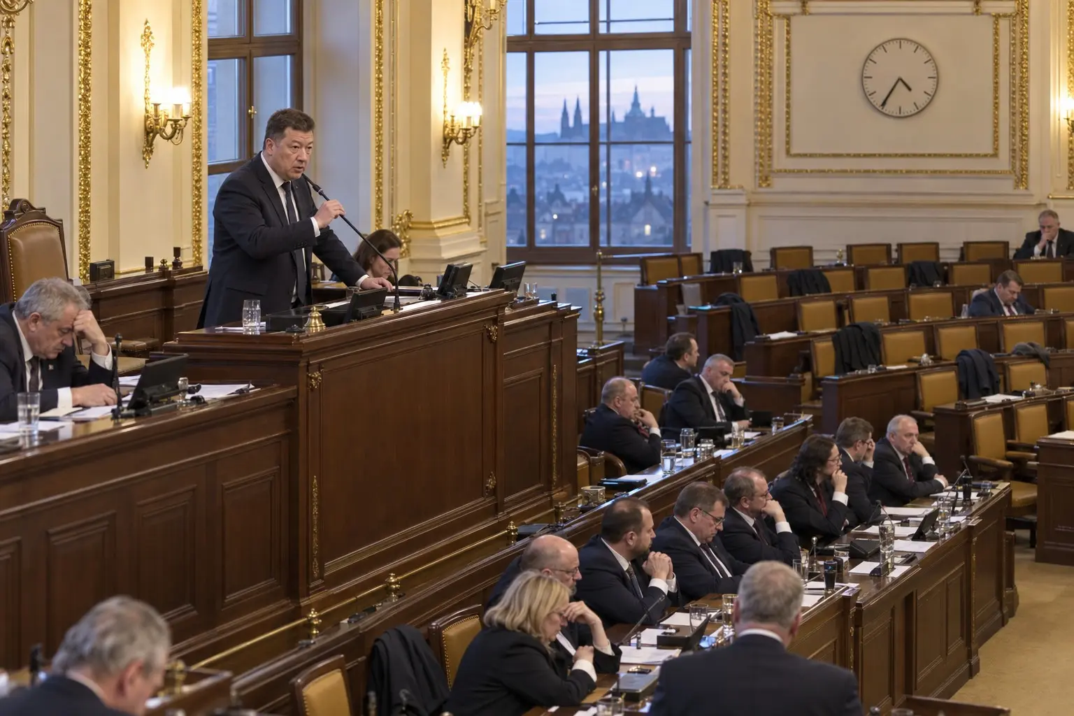 KI-generierte Illustration: Tomio Okamura am Präsidiumspult des tschechischen Abgeordnetenhauses bei Morgendämmerung, Regierungsbänke besetzt, Oppositionsbänke halb leer, Nachrichtenfoto-Stil.